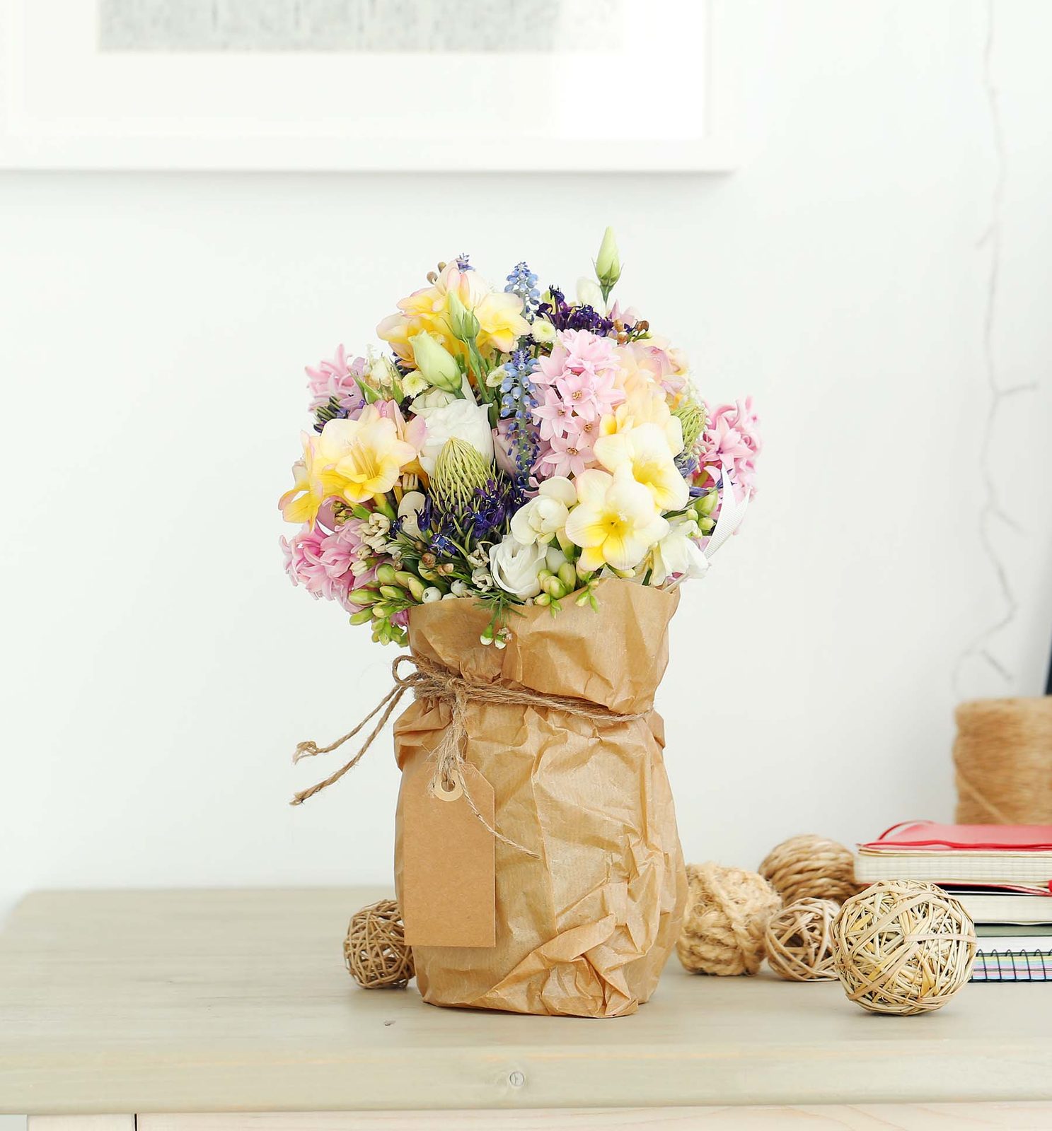 Handgebundener Strau&szlig; aus Pastellblumen in Kraftpapier auf einem hellen Sideboard